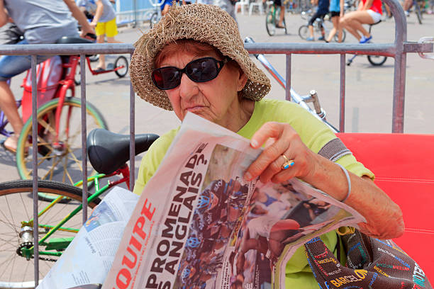 Nice, France - July 2, 2013; old woman reading l'Equipe, a French nationwide daily newspaper devoted to sports, on the Promenade des Anglais in Nice just before the start of the 4th stage of the Tour de France. Stage 4 was a team time trial that started and finished in Nice. The Australian team of Orica-GreenEdge was the fastest team over 25 kilometer.