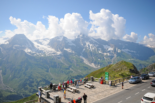 Grossglockner, Austria - July 21, 2013: Parking place on a viewing platform on the Grossglockner High Alpine Road (Salzburg, Austria). Cars parked. People wander around and enjoy the view. A couple on a information table about mountain names.
