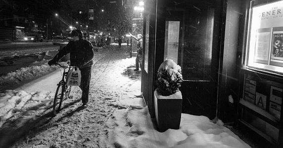 New York City, USA - January 21, 2014: Man with bicycle walking Bovery street under snowfall at night. Chinatown Manhattan, New York, USA.