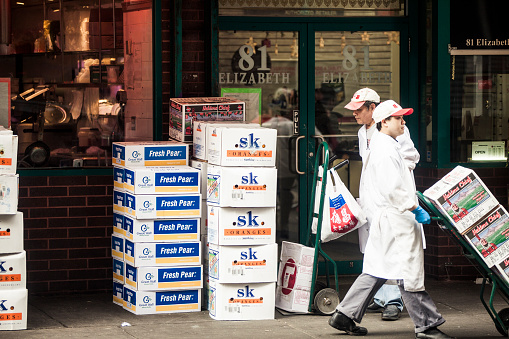 New York City, USA - April 19, 2013: Two grocerie store employes carrying a fruit delivery in Manhattan Chinatown's street.