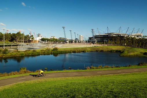 Sydney, Australia - January 27, 2014: A cyclist passes a lake and various sporting and entertainment venues in Sydney Olympic Park on a clear summer afternoon. 