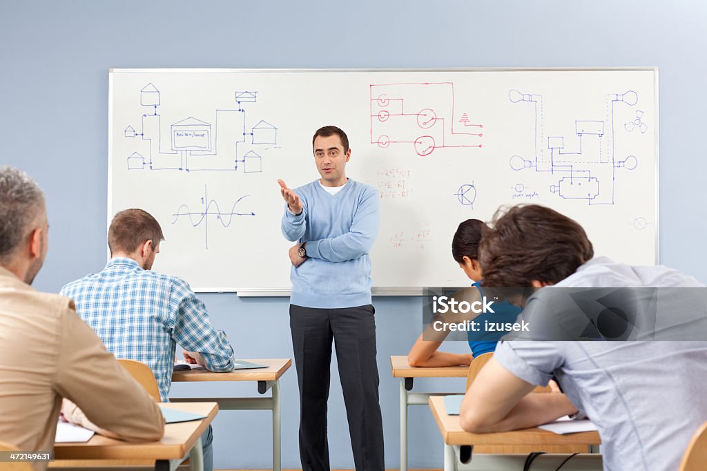 Adult Ed Group of adult student attending a job training. Male teacher explaining diagrams technical systems drawn on whiteboard. Electrician Stock Photo