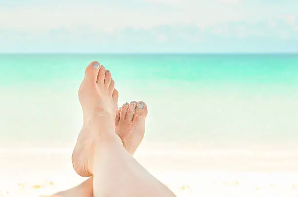 Woman with sandy feet and silver grey polish relaxing on a tropical beach