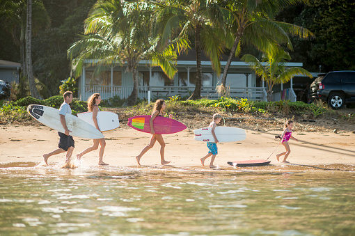 An active family on vacation in Hawaii at the beach on a sunny day going surfing and bodyboarding.