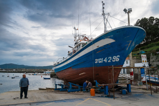 Corme, Spain - October 25, 2012: A sailor rests next to a boat in reparation at the harbor of the village. This small town is an important fishing villages in Galicia, northwestern Spain.