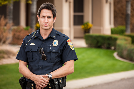 Portrait of a mid-adult caucasian male law enforcement police officer in uniform, standing in an affluent residential district.