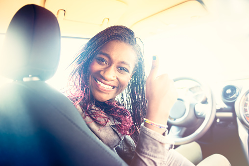 Young driver African woman inside of the car and holding thumb up .
