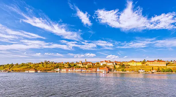 Panoramic wide angle view on the charming medieval city of Meersburg, located at the Lake Constance (Bodensee), with a sailing boat passing the city´s beautiful waterfront. 