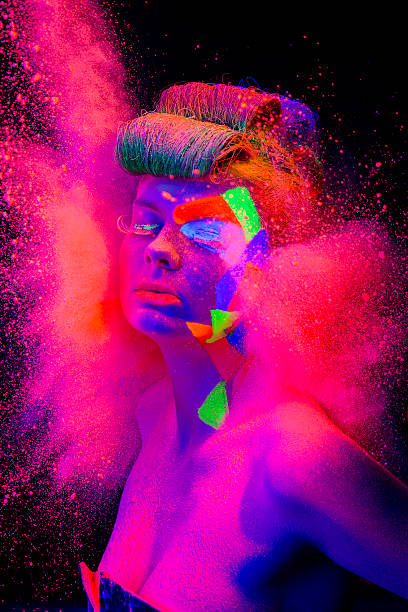 Women Portrait with Glowing makeup in black light Young women portrait in Neon Light with Multi Colored makeup an pink color powder explosion behind  crazy makeup stock pictures, royalty-free photos & images