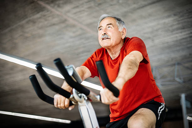 Senior Man on exercising Bicycle Healthy senior man in GYM cycling on exercising bicycle peloton exercise bike stock pictures, royalty-free photos & images