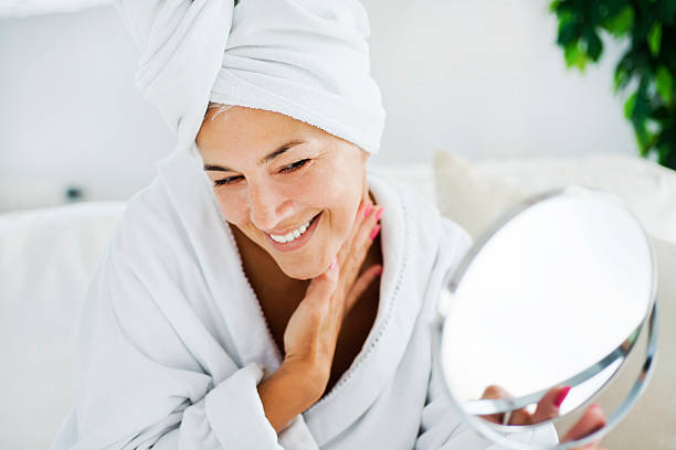 Mature woman and body care Beautiful mature woman applying a cream on her face after showering bathrobe photos stock pictures, royalty-free photos & images