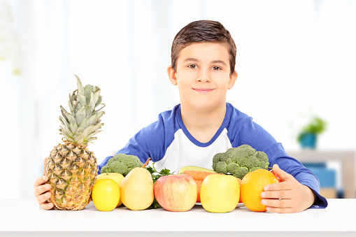 Smiling boy sitting at table full of fruits and vegetables