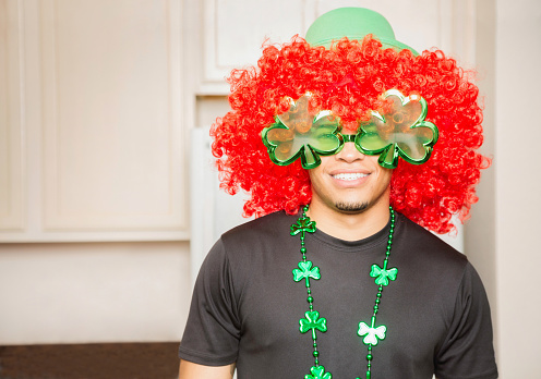 American hunk waring a fun disguise for a St-Patrick's day party with a huge red-head wig, green glasses and clover necklace.