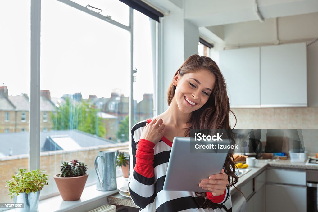 Girl using digital tablet Smiling beautiful brunette standing in the kitchen with a digital tablet in hand. Digital Tablet Stock Photo
