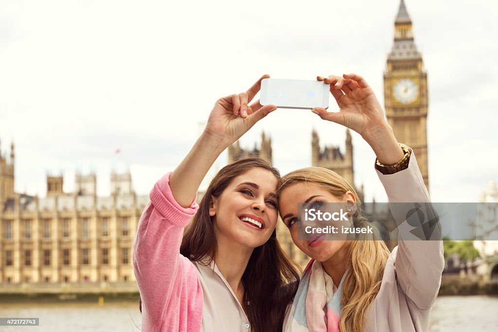 Friends in London Outdoor portrait of two happy women taking a self picture using a smart phone with Houses of Parliament and Big Ben in the background. 20-24 Years Stock Photo