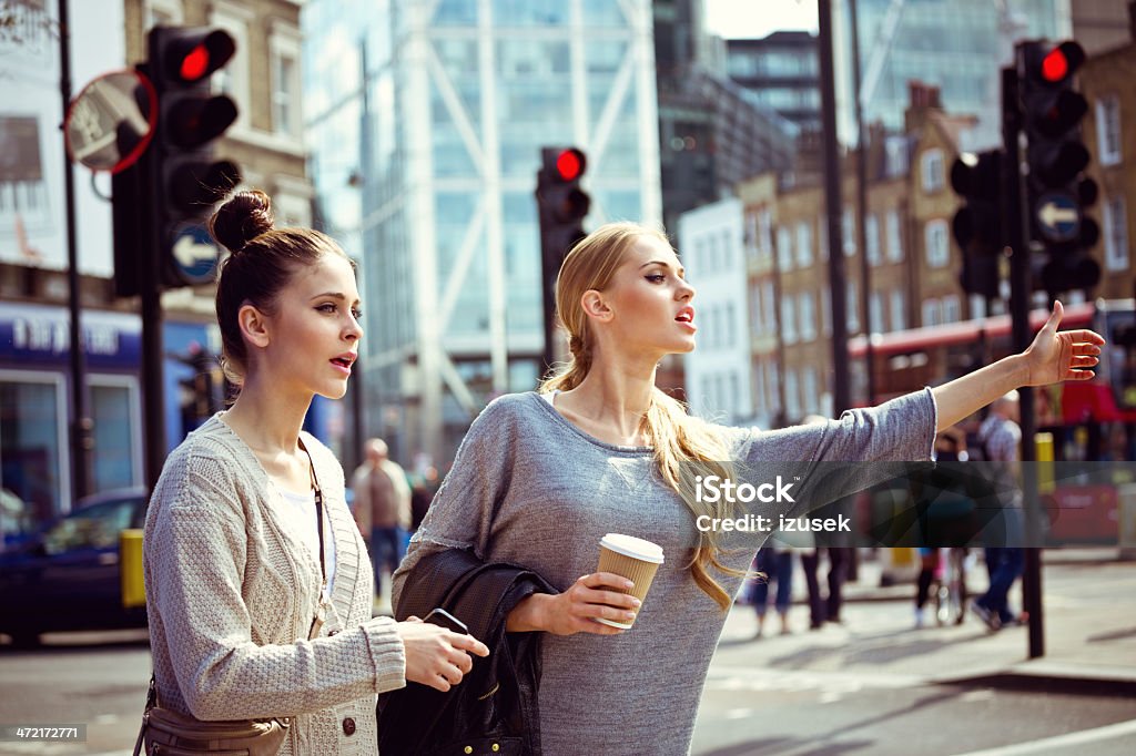 Hailing a taxi Two young women standing on the city street and hailing a taxi. 20-24 Years Stock Photo