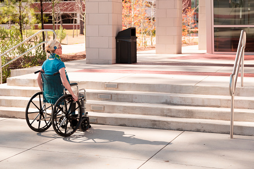 Disabled woman faced with inaccessble stairs to office or college building.  Civil rights violation, inequality for those with disabilities.  Facing adversity.