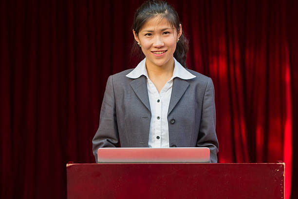 istock Smiling Asian Woman at Podium 472176039