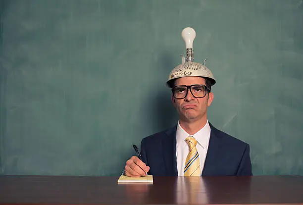 Photo of Confused Businessman Wearing Unlit Thinking Cap at Desk