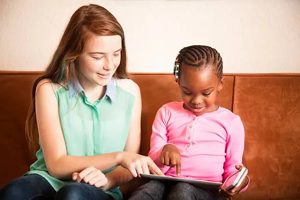 Photo of Baby sitter playing with preschooler using tablet mobile phone