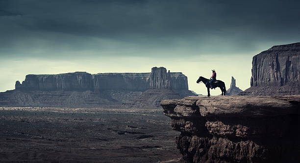 Native American Cowboy on Horse at Monument Valley Tribal Park Subject: A native American Indian cowboy riding on a horse over a cliff looking into the stormy distance. cumulonimbus photos stock pictures, royalty-free photos & images