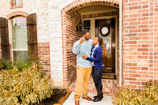 African descent couple shows off house key to their first home. Front door, entrance of this beautiful brick and stone home. 
