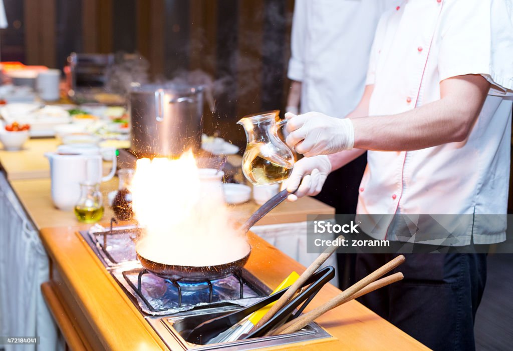 Flames Chef cooking in commercial kitchen, pouring white wine into frying pan Activity Stock Photo