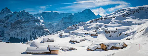 Traditional wooden Alpine chalets covered in a crisp white layer of fresh snow overlooked by the dramatic mountain peaks of the Bernese Alps, Switzerland. ProPhoto RGB profile for maximum color fidelity and gamut.