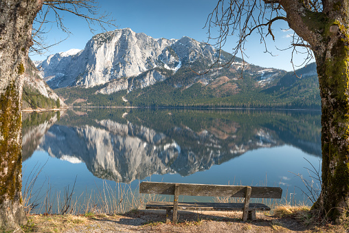 A wooden bench in front of a breathtaking panorama in the nature reserve Altaussee, a beautiful lake in the middle of the Austrian Alps. 