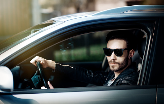 fashion male driving car and looking at camera, soft light, leather jacket, cool attitude,