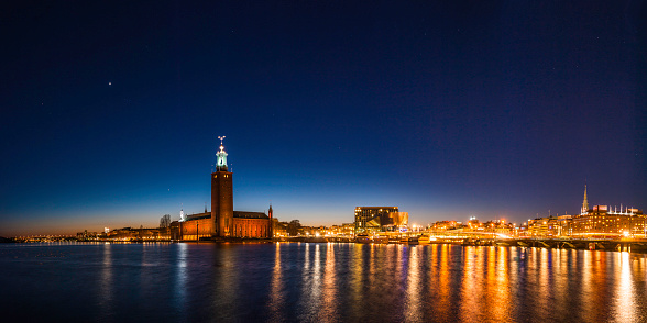 Stars shining in the deep blue panormic dusk skies over the iconic tower of Stockholm City Hall, Stadshuset, venue for the Nobel Prize banquet, the modern architecture of the downtown Norrmalm waterfront and Central station reflecting in the still waters of Riddarfjarden, Stockholm, Sweden. ProPhoto RGB profile for maximum color fidelity and gamut.