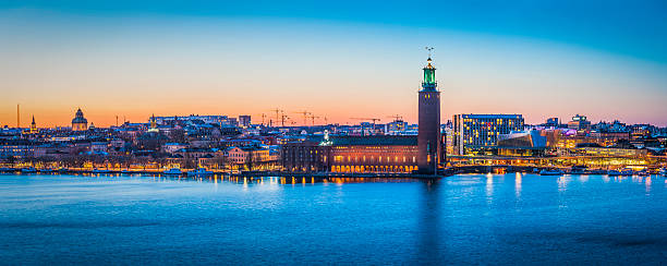 Stockholm sunset cityscape panorama over harbour City Hall waterfront Sweden Warm glow of midsummer sunset over the historic tower of Stockholm City Hall, Stadshuset, spotlit at its iconic waterfront location on Kungsholmen island reflecting in the still waters of Riddarfjarden in the heart of Sweden's picturesque capital city. ProPhoto RGB profile for maximum color fidelity and gamut. kungsholmen town hall photos stock pictures, royalty-free photos & images