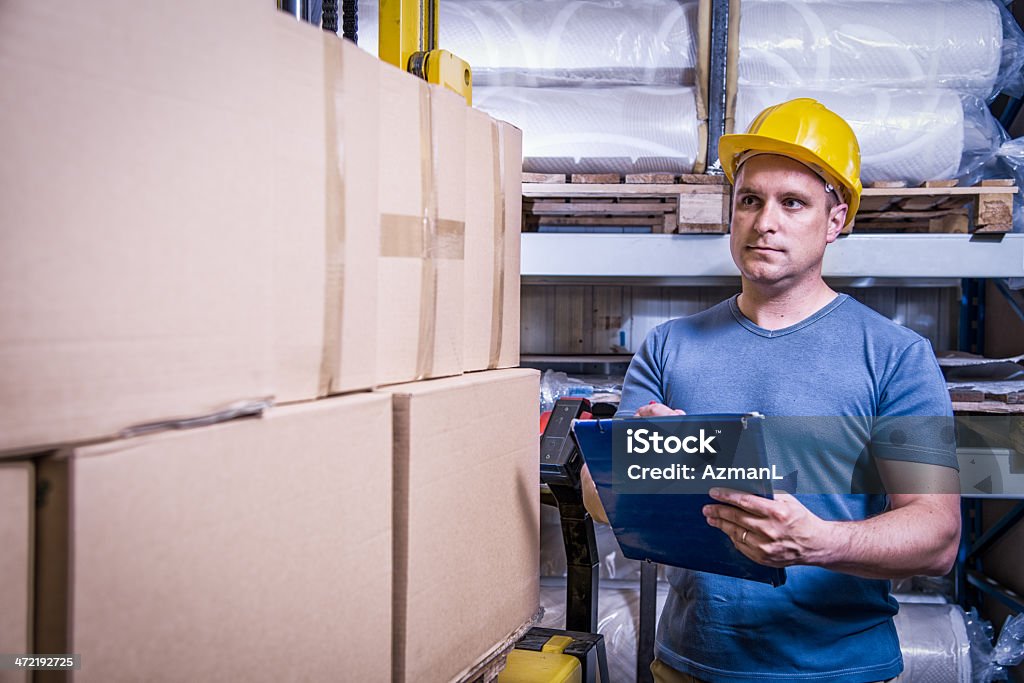 Worker checking shipment Worker in warehouse reviewing a warehouse shipment. Adult Stock Photo