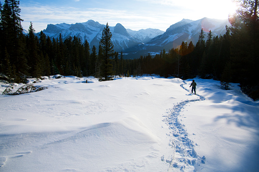 A woman enjoys a snowshoe adventure in the Rocky Mountains of Canada on a cold and sunny day.