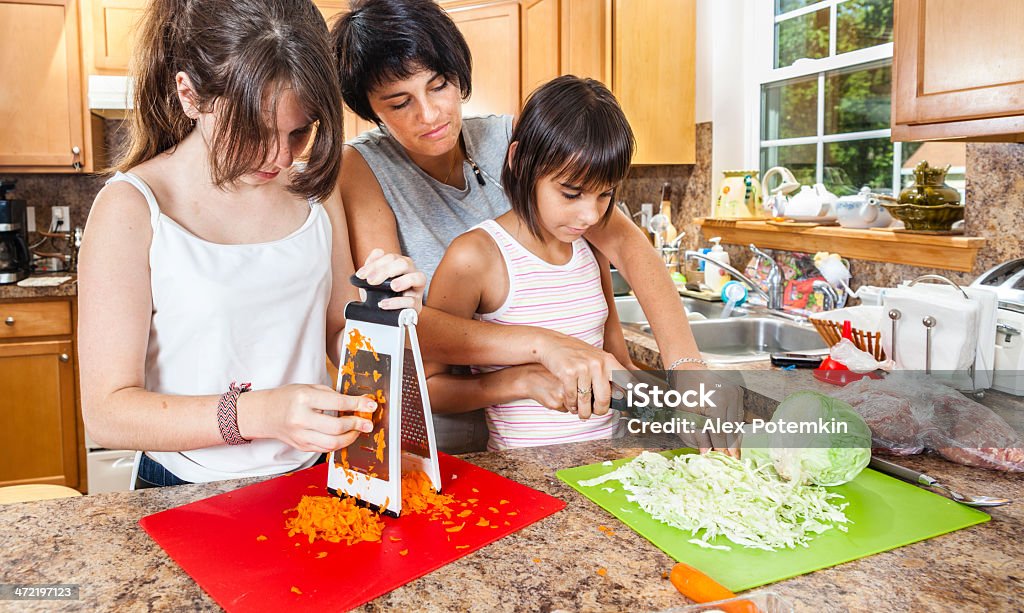 Family, mother with two daughters, cutting vegetables for salad Family, mother with two daughters, cutting vegetables, carrot and cabbage,  for salad  A Helping Hand Stock Photo