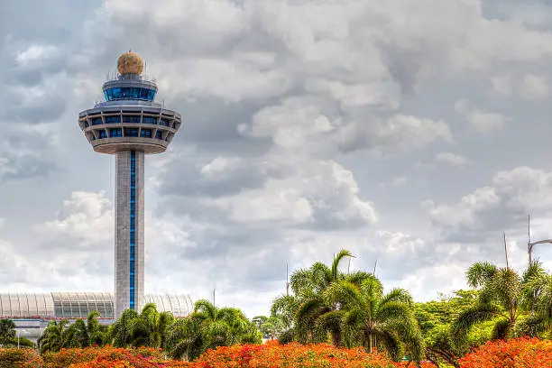 Singapore Changi International Airport Traffic Controller Tower with cloudy skies in the background and beautiful trees and shrubs in the foreground. The airport tower is one of the most recognizable icons of Singapore.