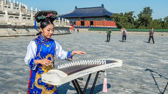 Beijing, China - October 14, 2014: A woman dressed in ancient chinese clothing playing the guzheng. Located in The Temple of Heaven, Beijing, China.