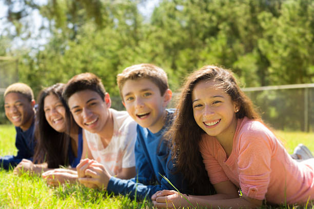 Teenagers: Mulit-ethnic group of friends together. Park or school campus. Diverse group of teenage friends hang out outside together at a local park or school campus. 13 14 years child teenage girls lying down stock pictures, royalty-free photos & images