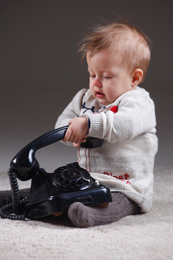 Toddler picking up the old black telephone.