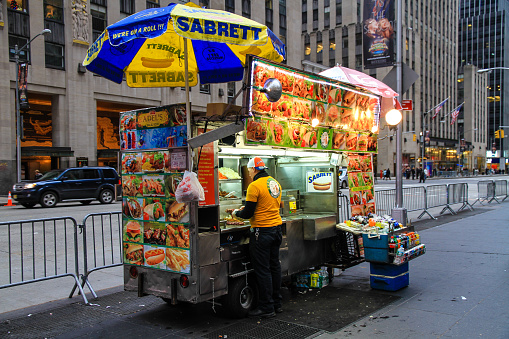 New York, USA - Dec 29, 2013: Fast food kiosk on New York street. Young man, vendor, preparing food for sale.