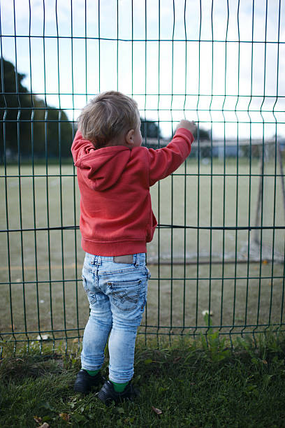 istock Little boy peering through a wire fence 472227005