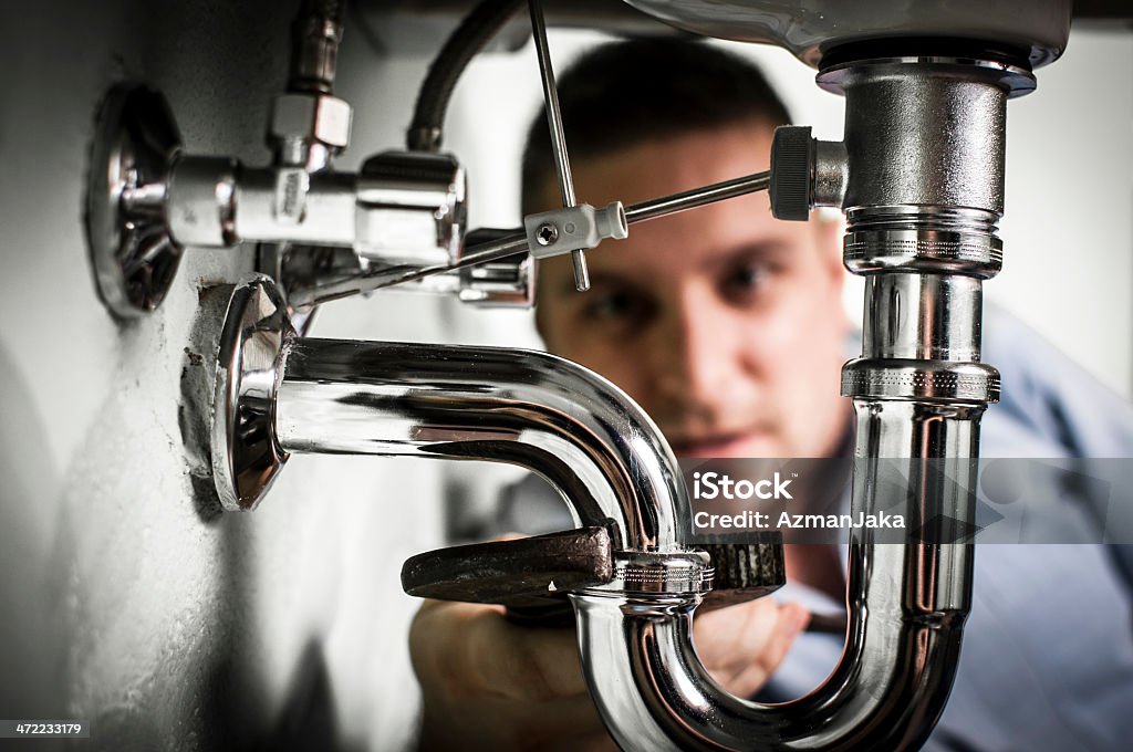 Plumber repairing sink Plumber doing some work under the sink. Tightening siphon. Below Stock Photo