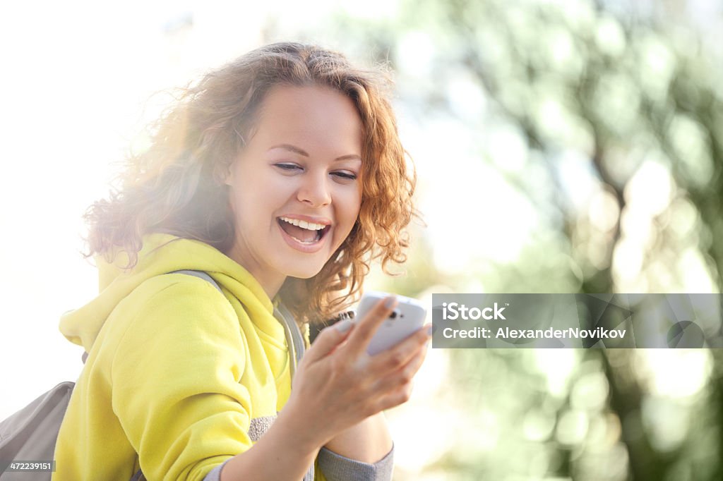 Young woman viewing something on her smartphone and smiling Happy Young Woman is Viewing Photos on her Mobile Phone in the Bright Spring Day 16-17 Years Stock Photo
