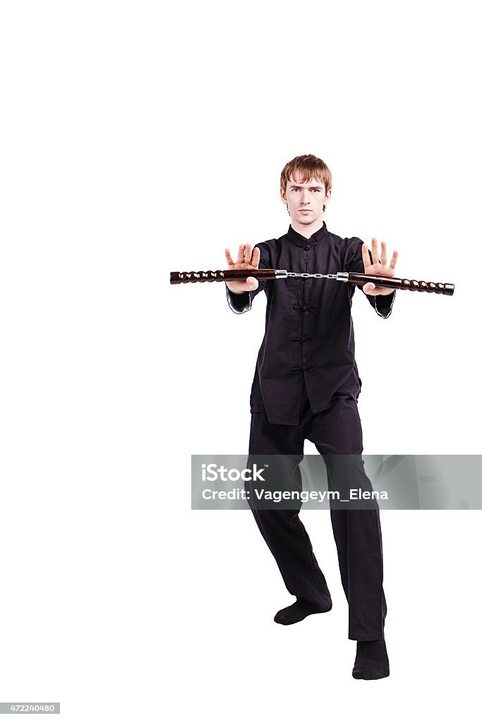 Man in a kimono practicing kung fu with nunchaku The man in a kimono practicing kung fu. The wizard displays a nunchaku kata. Fighter isolated on white background. Concept of healthy life and martial arts. Nunchaku Stock Photo