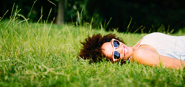 Smiling young african american woman lying on green grass