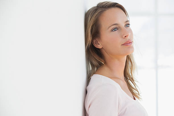 istock Happy blonde woman leaning against wall thinking 472242467