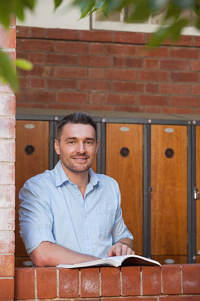 istock Smiling male student holding a book in college corridor 472242563