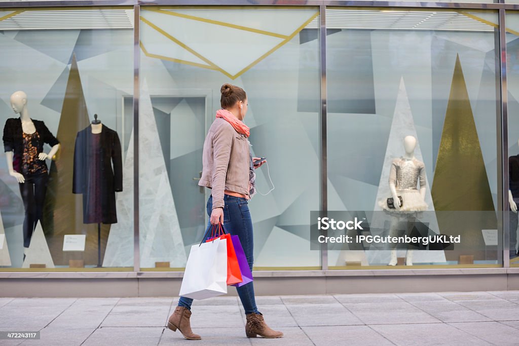 Young woman with shopping bags looking at window display Profile shot of young woman with shopping bags looking at window display Window Shopping Stock Photo