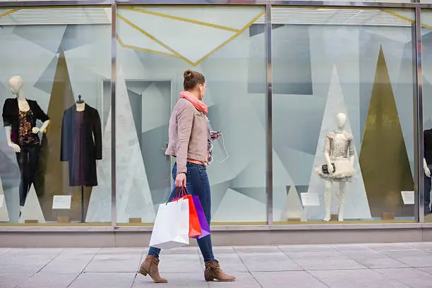 Photo of Young woman with shopping bags looking at window display