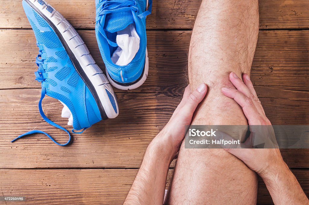 Injured runner Unrecognizable injured runner sitting on a wooden floor background Running Stock Photo